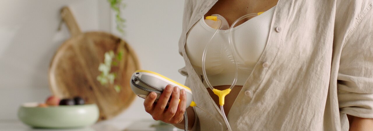 A mãe a usar a bomba tira leite eléctrica dupla e portátil Medela Freestyle™ mãos-livres, mostrando como os copos de recolha cabem facilmente no sutiã