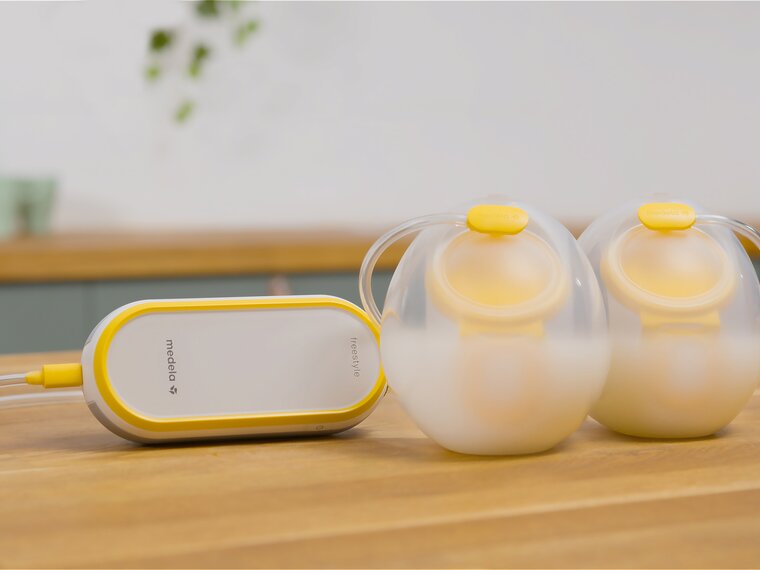 Medela Freestyle™ Hands-free double electric wearable breast pump sitting on counter with collection cups filled with milk