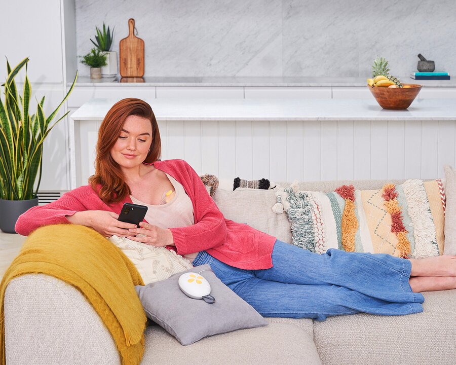 Mom using her phone while resting on a couch and using her Medela Solo™ Hands-free single electric breast pump