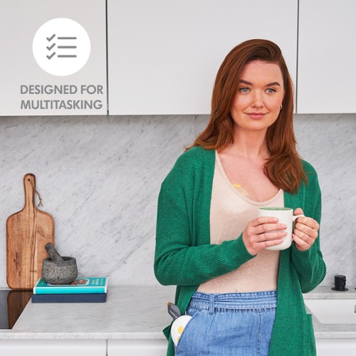 Mama drinkt koffie terwijl ze in de keuken staat met haar Medela Solo™ Hands-free enkele elektrische borstkolf. De tekst op de afbeelding luidt: “Ontworpen voor multitasking. | © Solo™ Hands-free single electric breast pumps