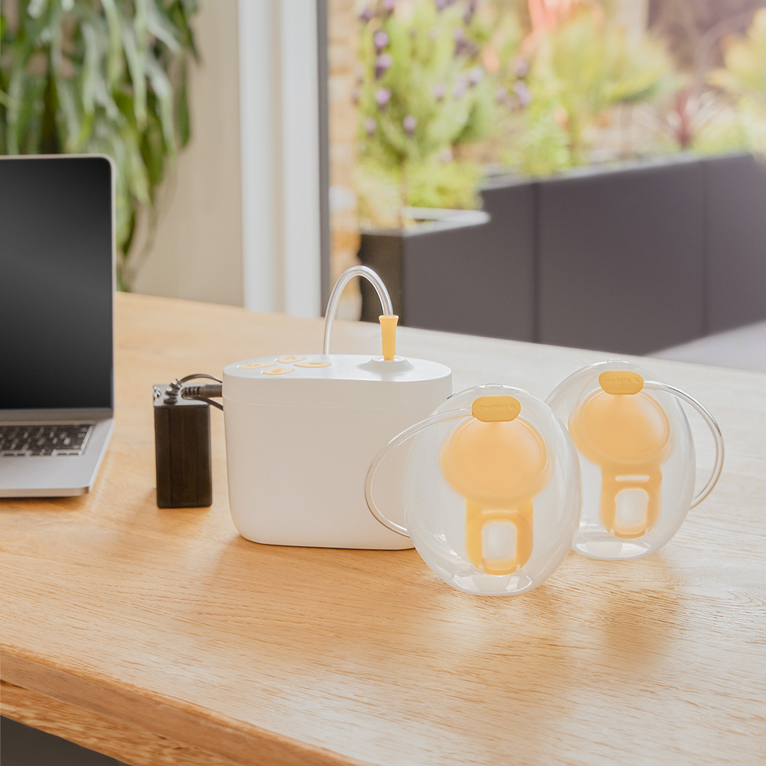 Medela Pump In Style® Hands-free double electric breast pump sitting on office desk with the pump, Hands-free collection cups and battery pack charger