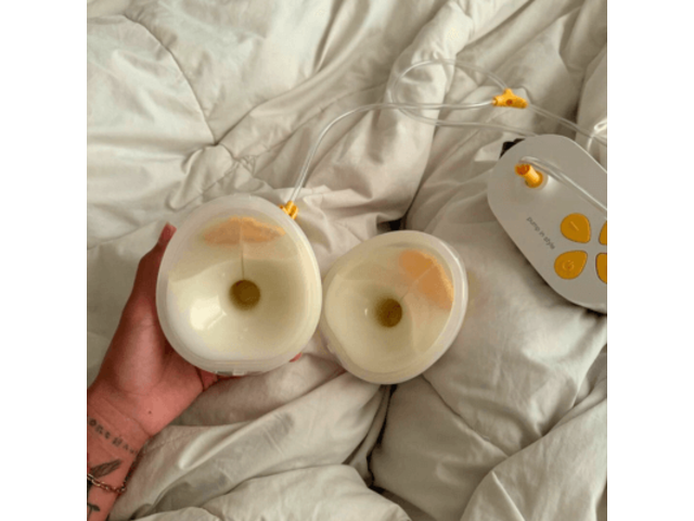 Pump In Style Hands-free breast pump with full collection cups sitting on white down comforter.