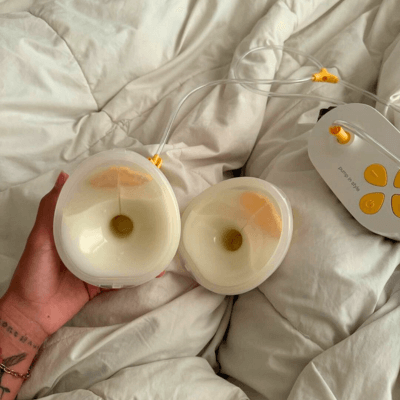 Pump In Style Hands-free breast pump with full collection cups sitting on white down comforter.