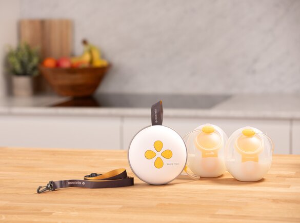 Medela Swing Maxi™ double electric breast pump on counter with lanyard and a set of filled Hands-free Collection Cups.
