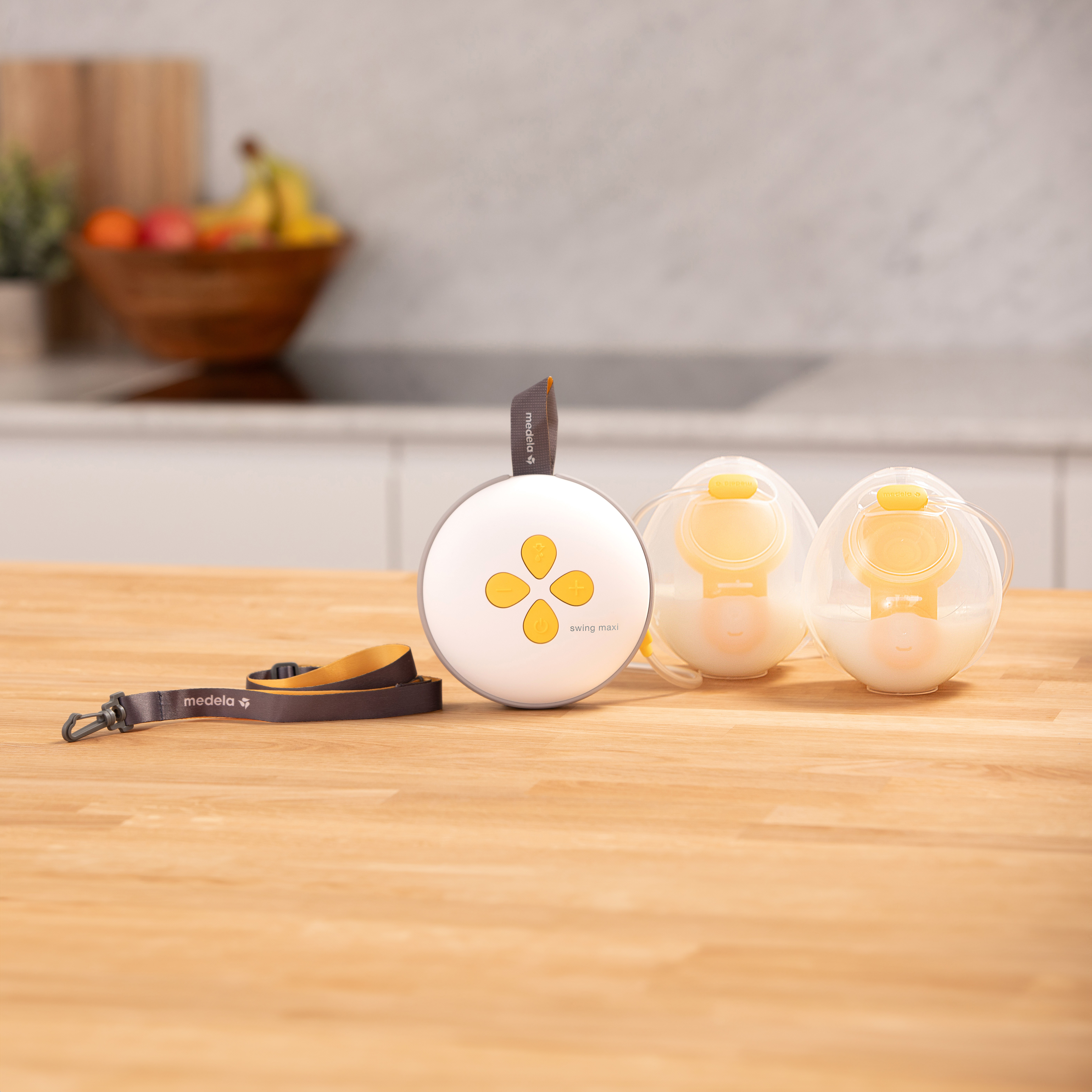 Medela Swing Maxi™ elektrische Doppelmilchpumpe auf der Theke mit Trageband und einem Satz gefüllter Hands-free Collection Cups.