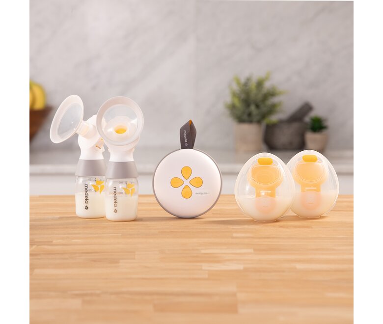 Medela Swing Maxi™ double electric breast pump on counter with two Classic collection containers and two Hands-free collection cups.