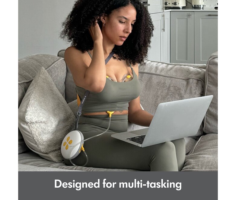 Woman sitting on couch using laptop while pumping with the Medela Swing Maxi™ double electric breast pump.  Text at bottom of image says, "Designed for multi-tasking"