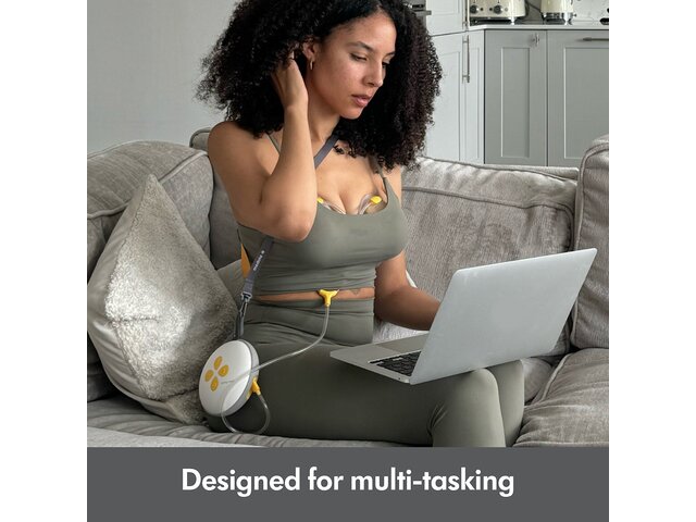 Woman sitting on couch using laptop while pumping with the Medela Swing Maxi™ double electric breast pump.  Text at bottom of image says, "Designed for multi-tasking"