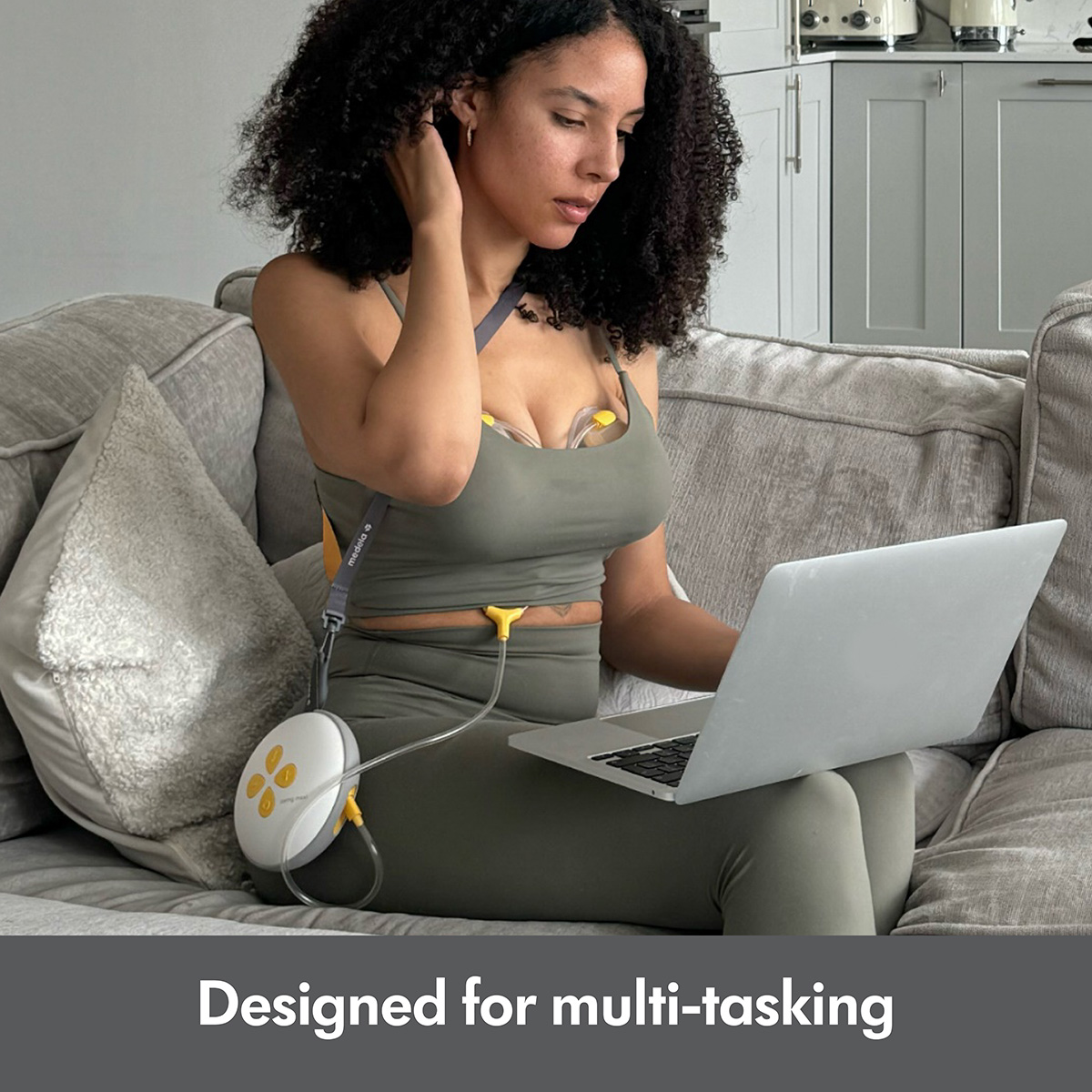 Woman sitting on couch using laptop while pumping with the Medela Swing Maxi™ double electric breast pump.  Text at bottom of image says, "Designed for multi-tasking"