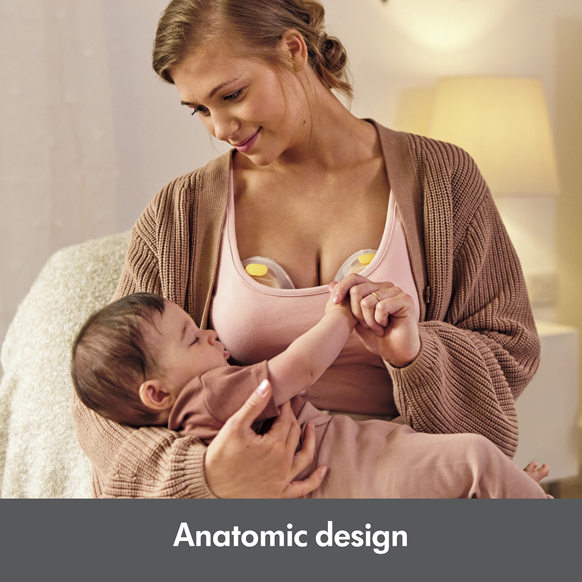 Woman holding baby while pumping with the Medela Swing Maxi™ double electric breast pump.  Text at bottom of image says, "Anatomic design"