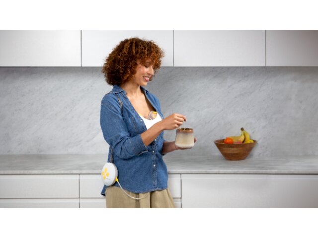 Mamma che indossa un tiralatte elettrico doppio Medela Swing Maxi™ mentre beve il caffè del mattino in cucina.