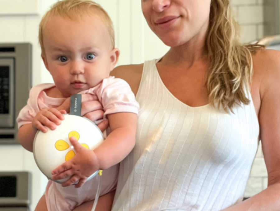 Woman standing and holding her baby while she wears Swing Maxi Hands-free breast pump.
