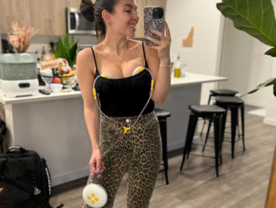 Woman standing in kitchen taking a selfie while pumping with Swing Maxi hands-free breast pump.
