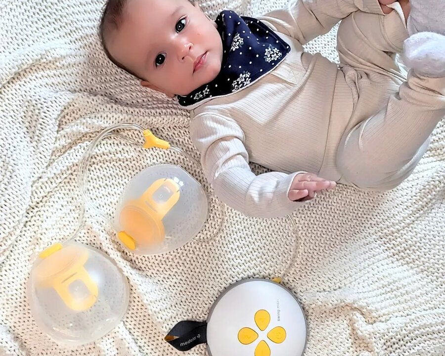 Baby laying on blanket next to Medela Swing Maxi Hands-free breast pump.