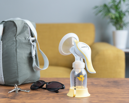The Medela Harmony™ manual breast pump on a table at home ready to go with keys, glasses and diaper bag.
