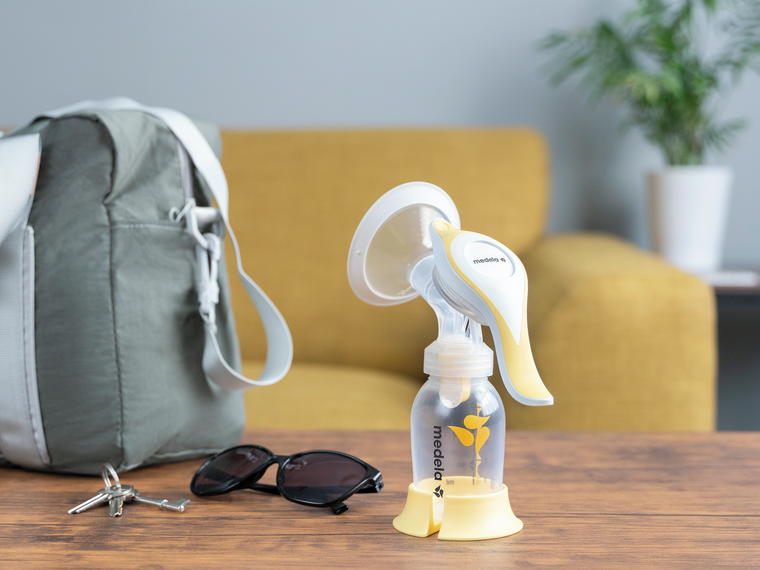 The Medela Harmony™ manual breast pump on a table at home ready to go with keys, glasses and diaper bag.