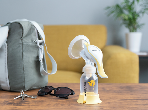 The Medela Harmony™ manual breast pump on a table at home ready to go with keys, glasses and diaper bag.