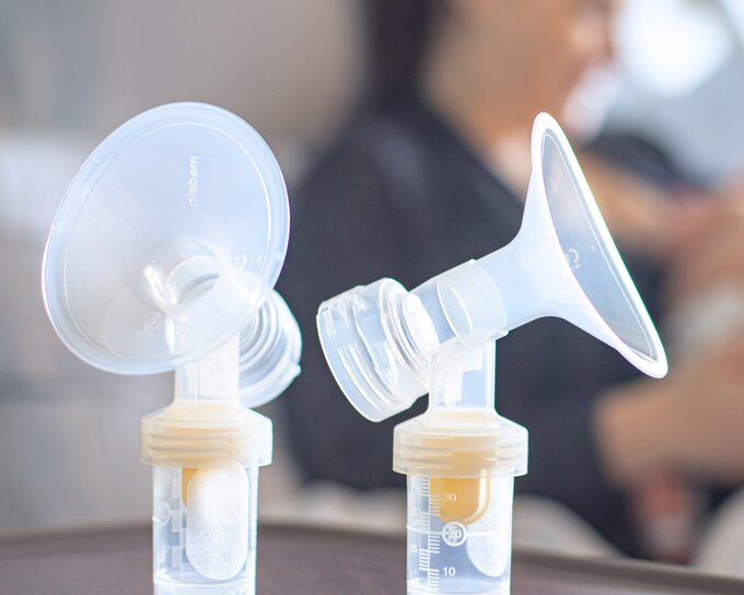 Mom feeding her newborn in a hospital bed with a sterile breast pump set from Medela in the foreground