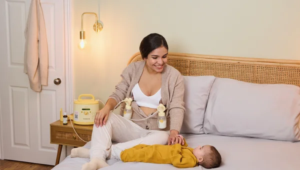La mamma pompa con il suo tiralatte Medela Symphony PLUS® noleggiato mentre gioca con il suo bambino.