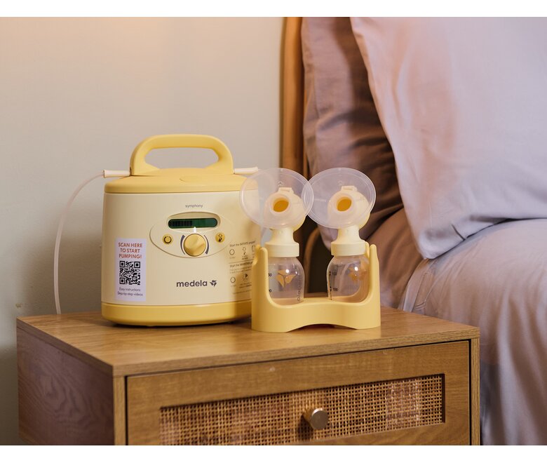 Die Medela Symphony PLUS® Milchpumpe und ein Abpumpset zu Hause auf dem Nachttisch.