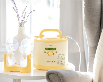 Uma bomba tira leite Medela Symphony PLUS® e um kit de bombagem estão em cima da mesa em casa.