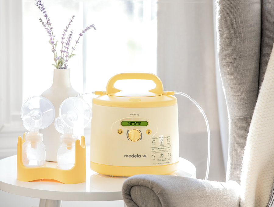 Uma bomba tira leite Medela Symphony PLUS® e um kit de bombagem estão em cima da mesa em casa.