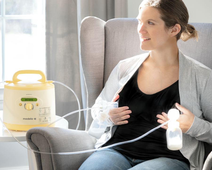 Eine Mutter plaudert in ihrem Wohnzimmer zu Hause, während sie mit ihrer gemieteten Medela Symphony PLUS® Milchpumpe abpumpt.