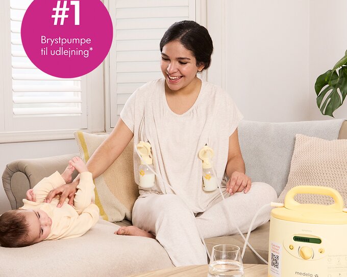 Mor på sofaen med baby, mens hun pumper med en lejet Medela Symphony®-brystpumpe. Billedtekst: »#1 Brystpumpe til udlejning"