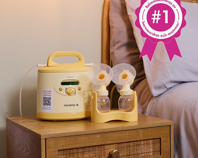 En Medela Symphony®-bröstpump på ett nattduksbord. Text på rosa märke: ”#1 Rekommenderad av barnmorskor och mammor”.