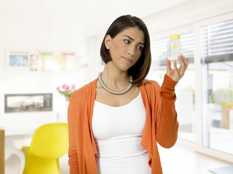 A mom looking at the low level of breast milk in a breast milk storage bottle