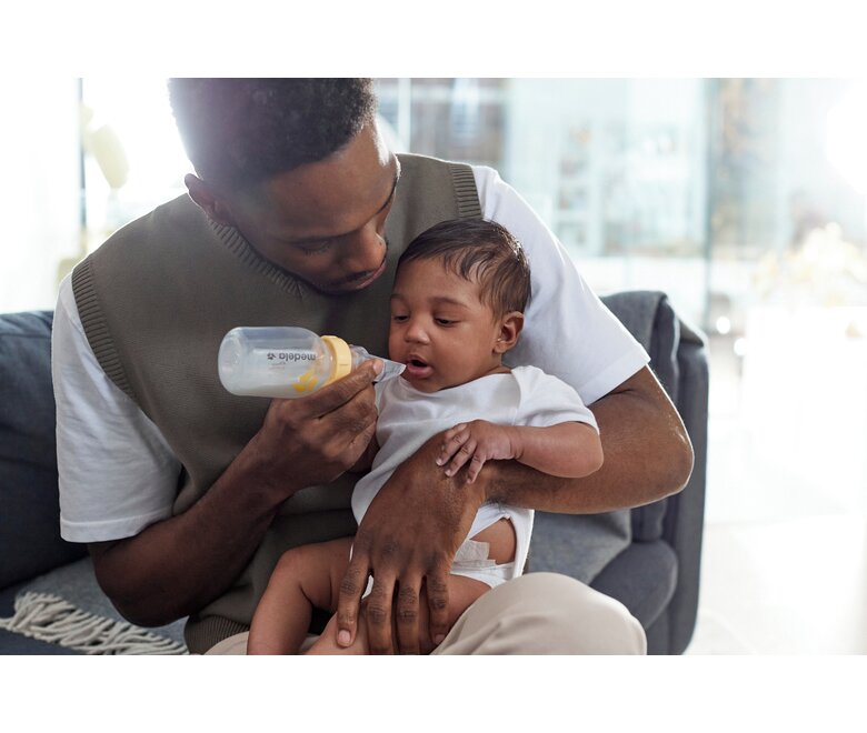 A baby is fed by his dad with a Medela Softcup™.