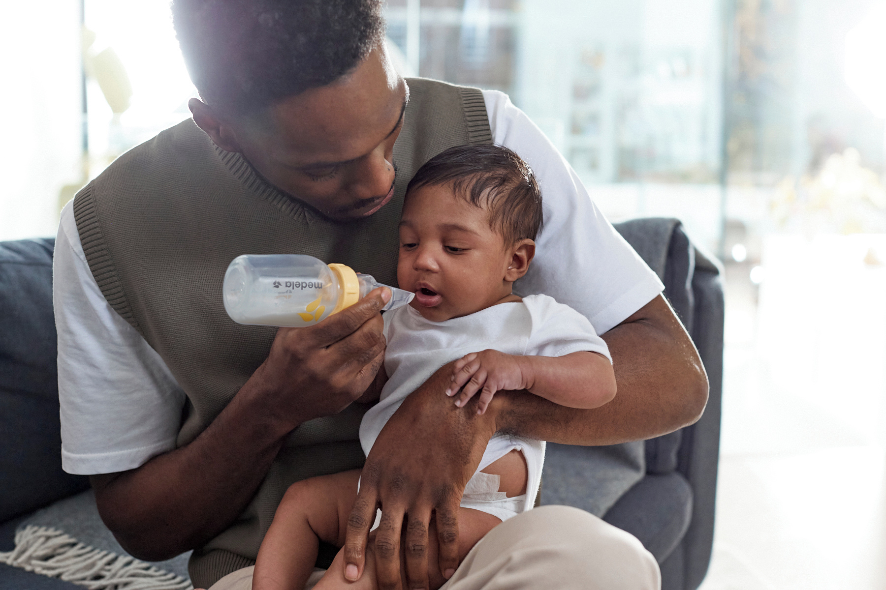 A baby is fed by his dad with a Medela Softcup™.