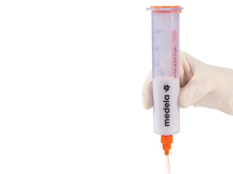 Medela GraviFeed® Syringes with ENFit® Connectors A Medela GraviFeed® Syringe with ENFit® Connector and tubing held by someone's hand wearing a surgical glove.