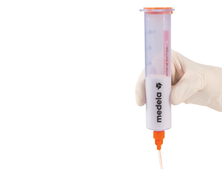 A Medela GraviFeed® Syringe with ENFit® Connector and tubing held by someone's hand wearing a surgical glove.