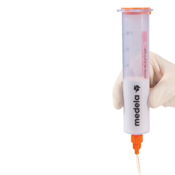 A Medela GraviFeed® Syringe with ENFit® Connector and tubing held by someone's hand wearing a surgical glove.