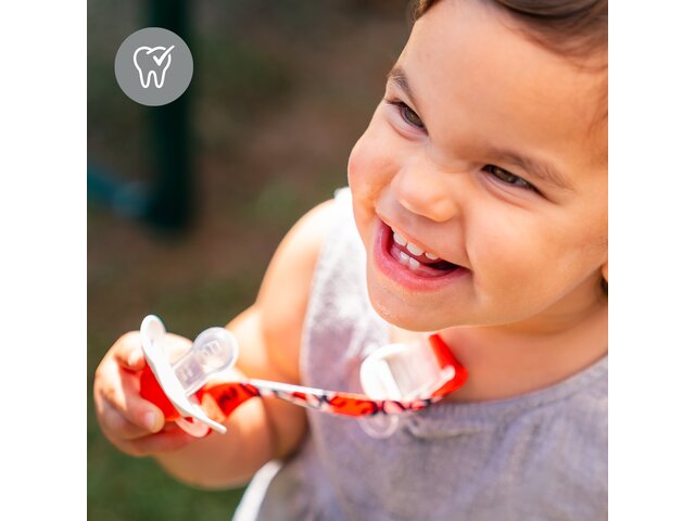 Happy baby holding a dummy attached to clothes. Icon on image: "Orthodontic design"