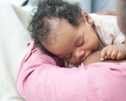 A baby breastfeeding on its mom's lap while at home.