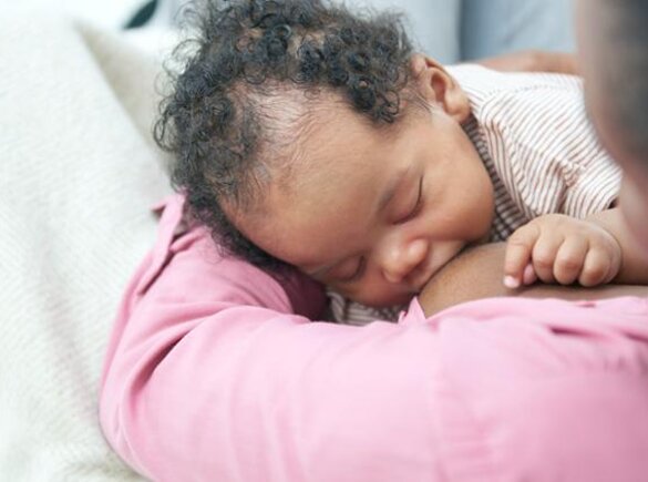 A baby breastfeeding on its mom's lap while at home.