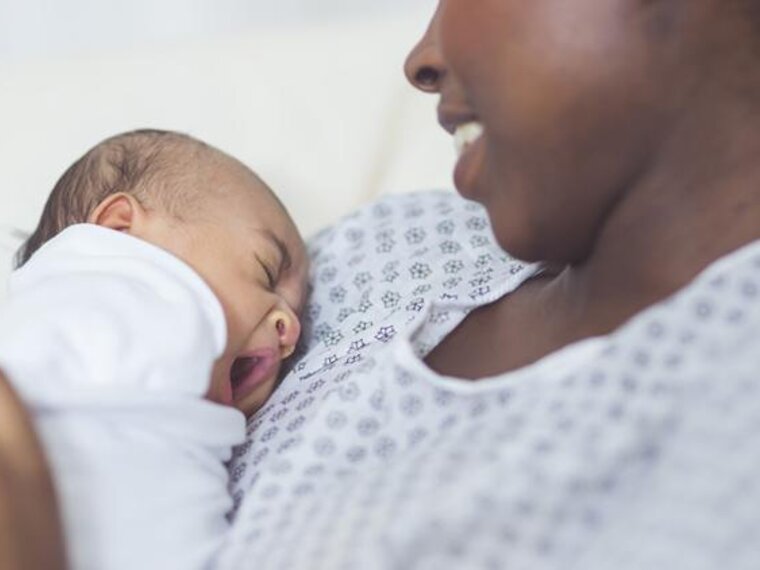 A smiling mom sits in a hospital with her newborn baby on her chest.