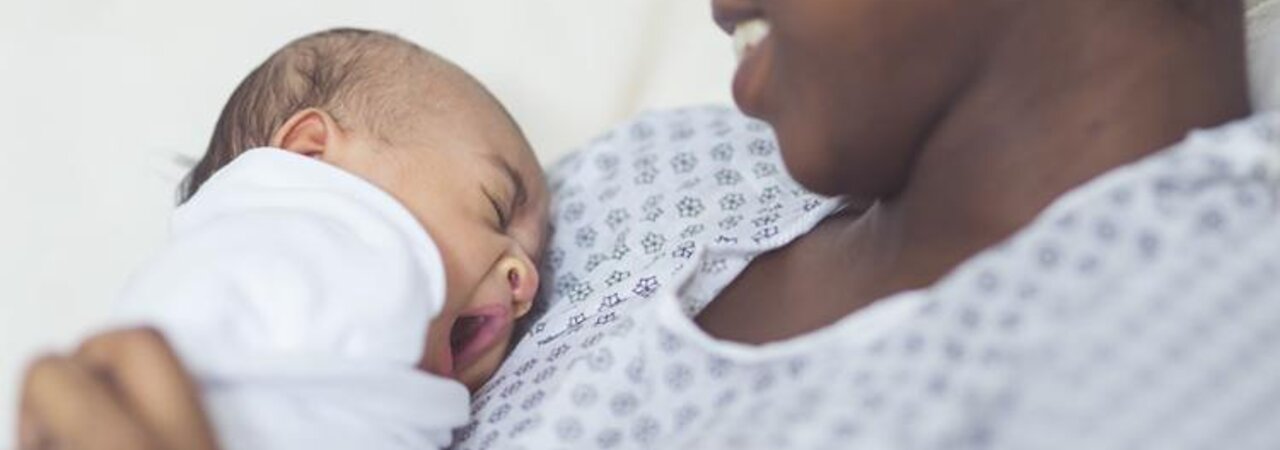 Une maman souriante est assise dans un hôpital avec son nouveau-né sur la poitrine.