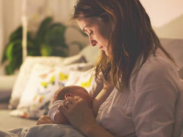 A mom breastfeeding her baby at night in her living room with the lights dimmed.
