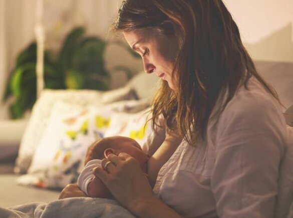 A mom breastfeeding her baby at night in her living room with the lights dimmed.