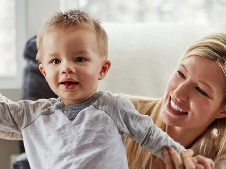 A smiling mom helps a boy learn to stand, then walk.