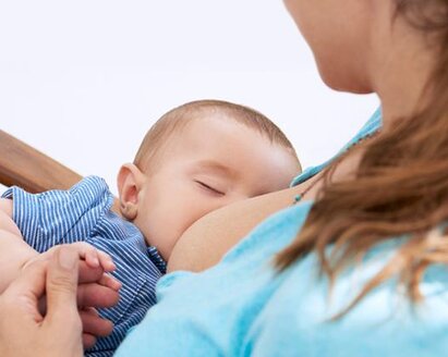 A baby falls asleep while being breastfed in his mother's arms as she sits in a rocking chair.