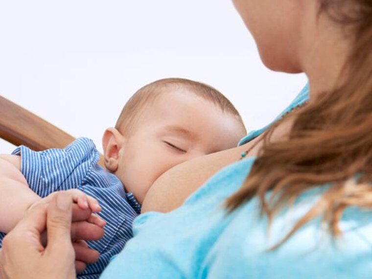 A baby falls asleep while being breastfed in his mother's arms as she sits in a rocking chair.