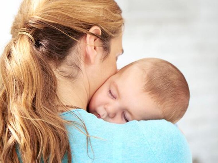 A mother holds her baby close to her body as it sleeps in her arms.