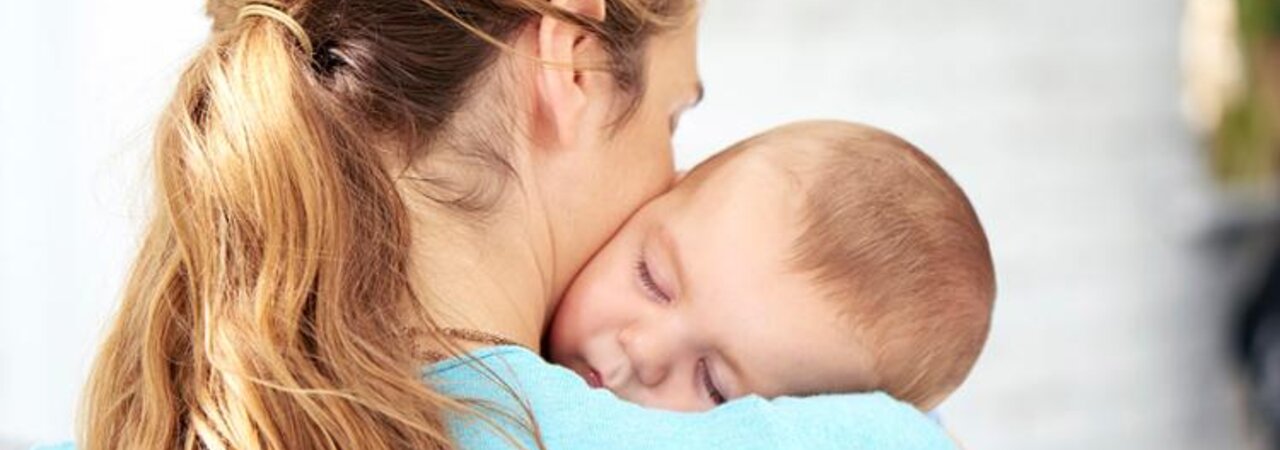 A mother holds her baby close to her body as it sleeps in her arms.