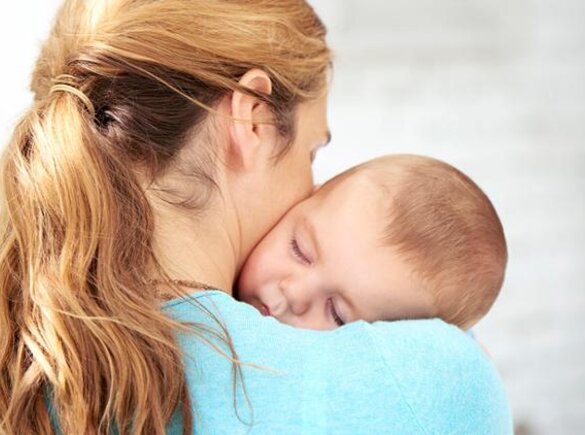 A mother holds her baby close to her body as it sleeps in her arms.