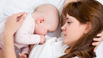 A mom watches as her baby sleeps in the bed next to her.