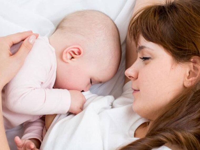 A mom watches as her baby sleeps in the bed next to her.
